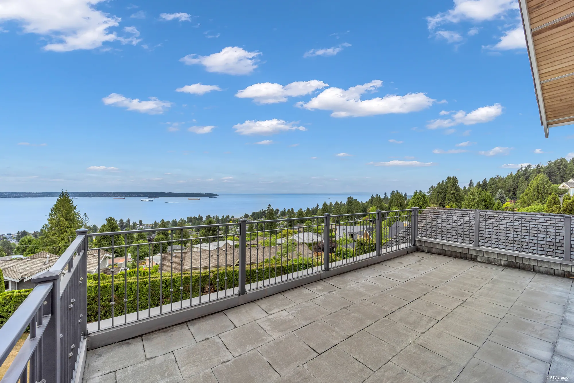 The main balcony running the width of the house in stone paving behind a black metal rail, the inlet filling the whole opening