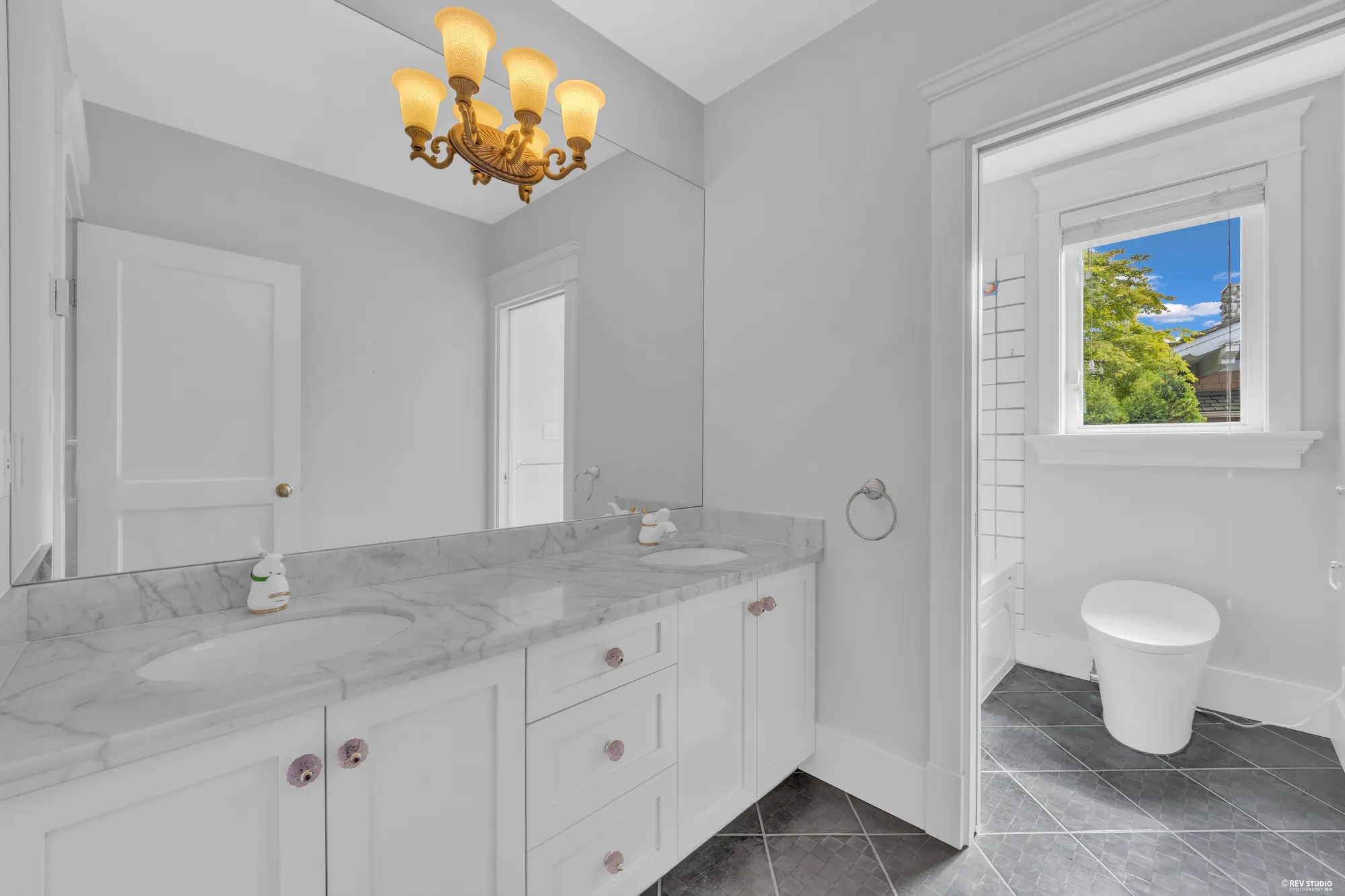 An upstairs bathroom with a white vanity, a marble top and a window over the tub