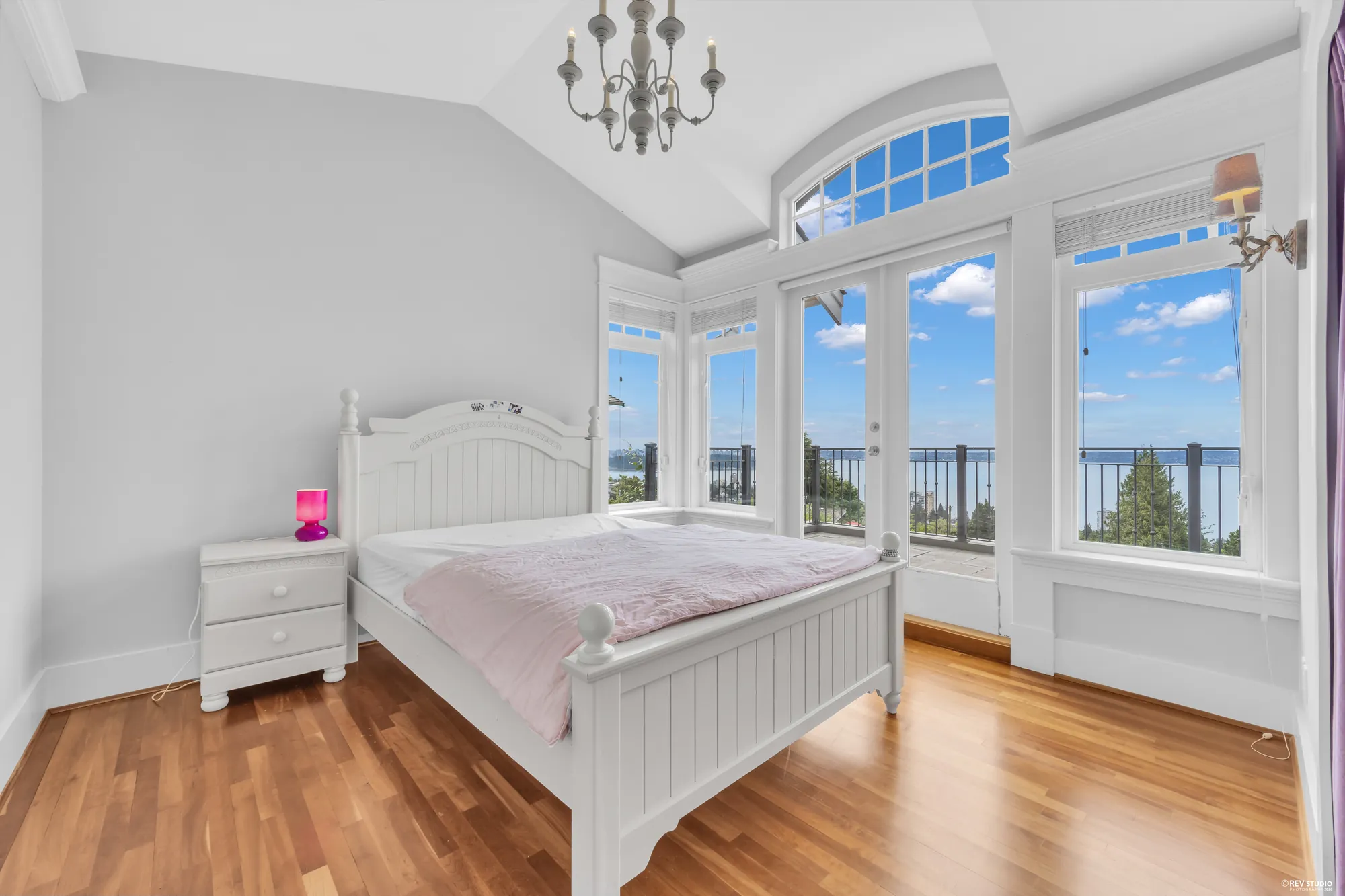 A bedroom in a bay of windows facing the water, a white-painted bed under the arched transom