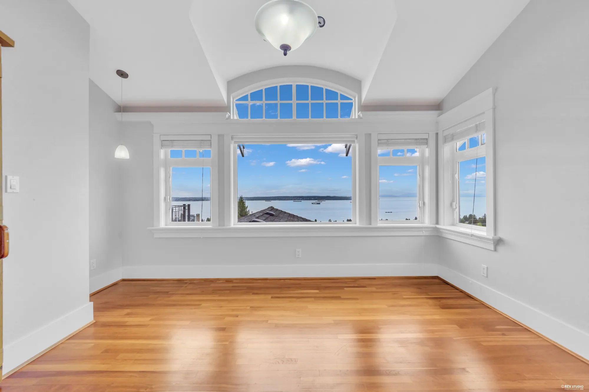 An unfurnished bedroom with an arched transom over the window and cherry floors