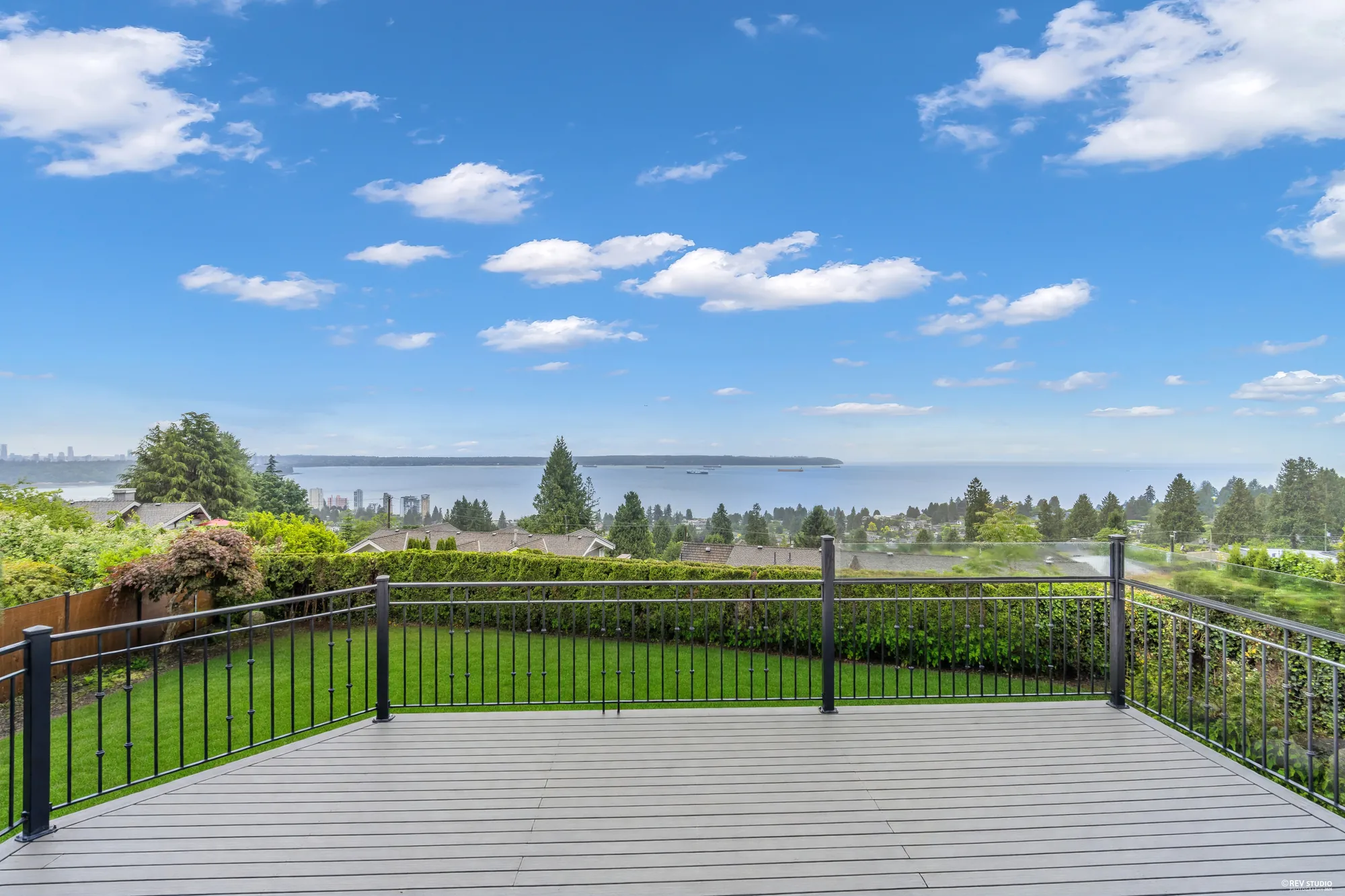 The deck from the lawn with the boundary hedge behind it and the water past the rail