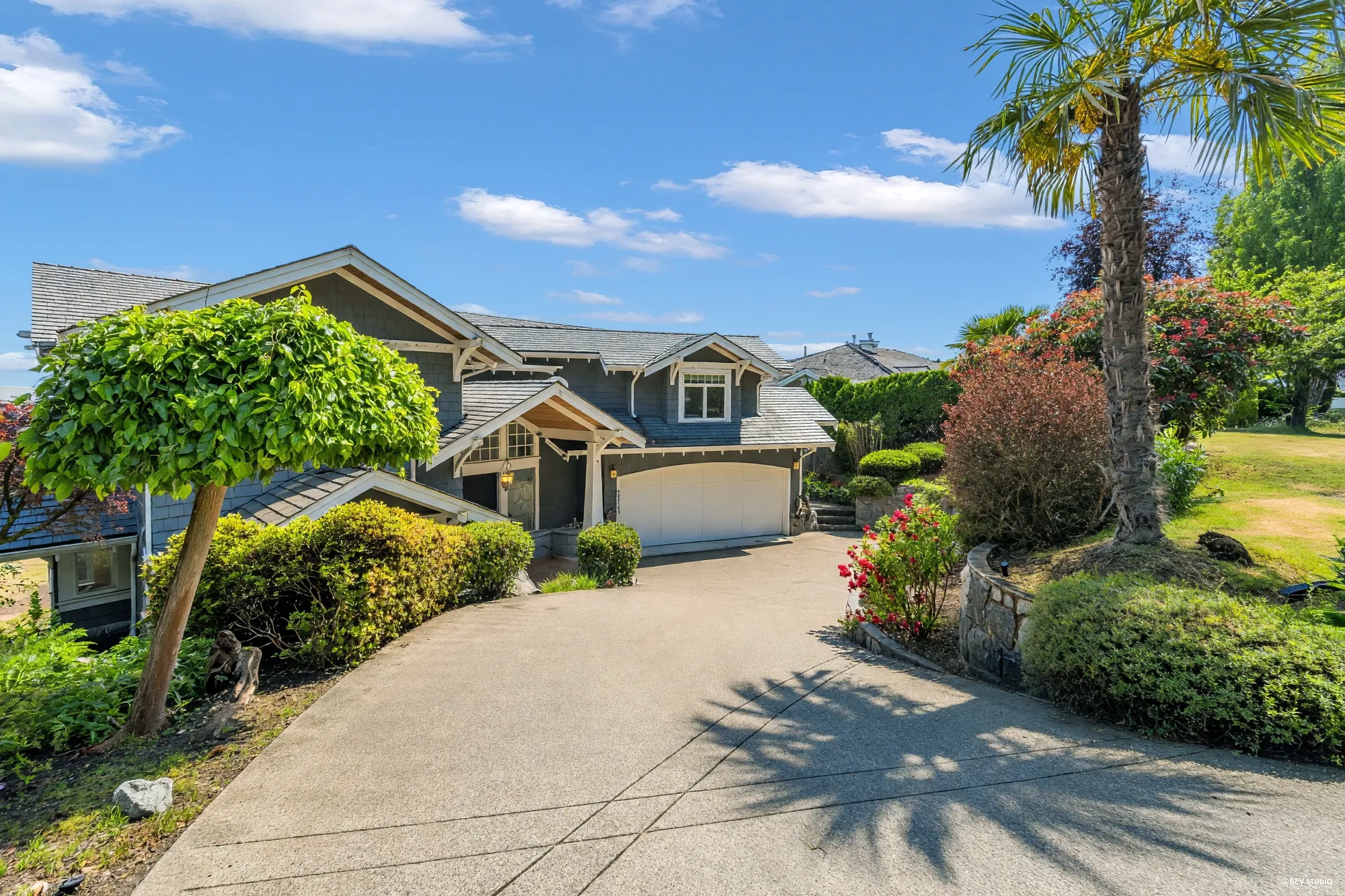 The turning circle in front of the garage with a mature palm, clipped hedges and a stone retaining wall