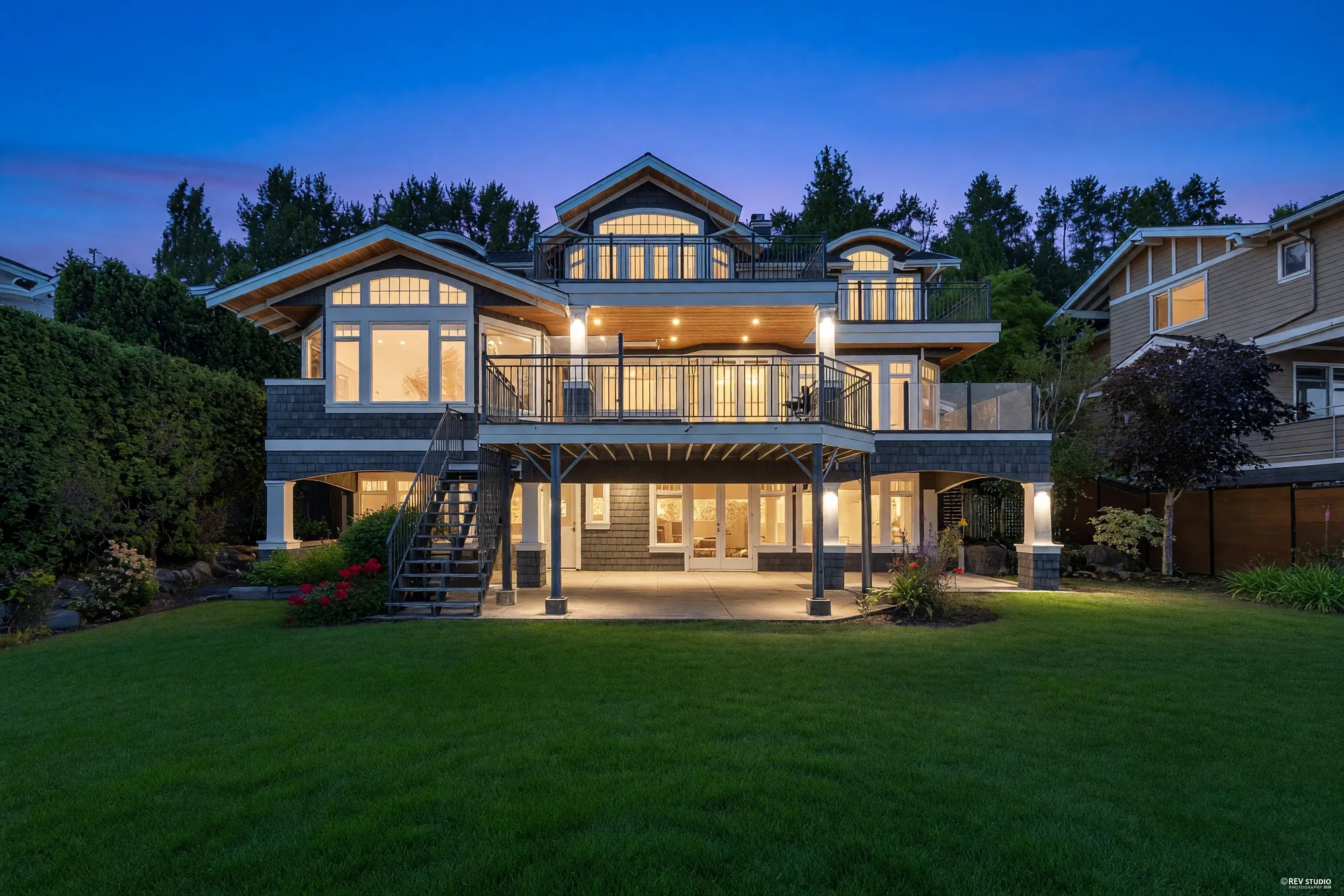 The back of the house at dusk from the lawn, three storeys of lit windows above the covered patio