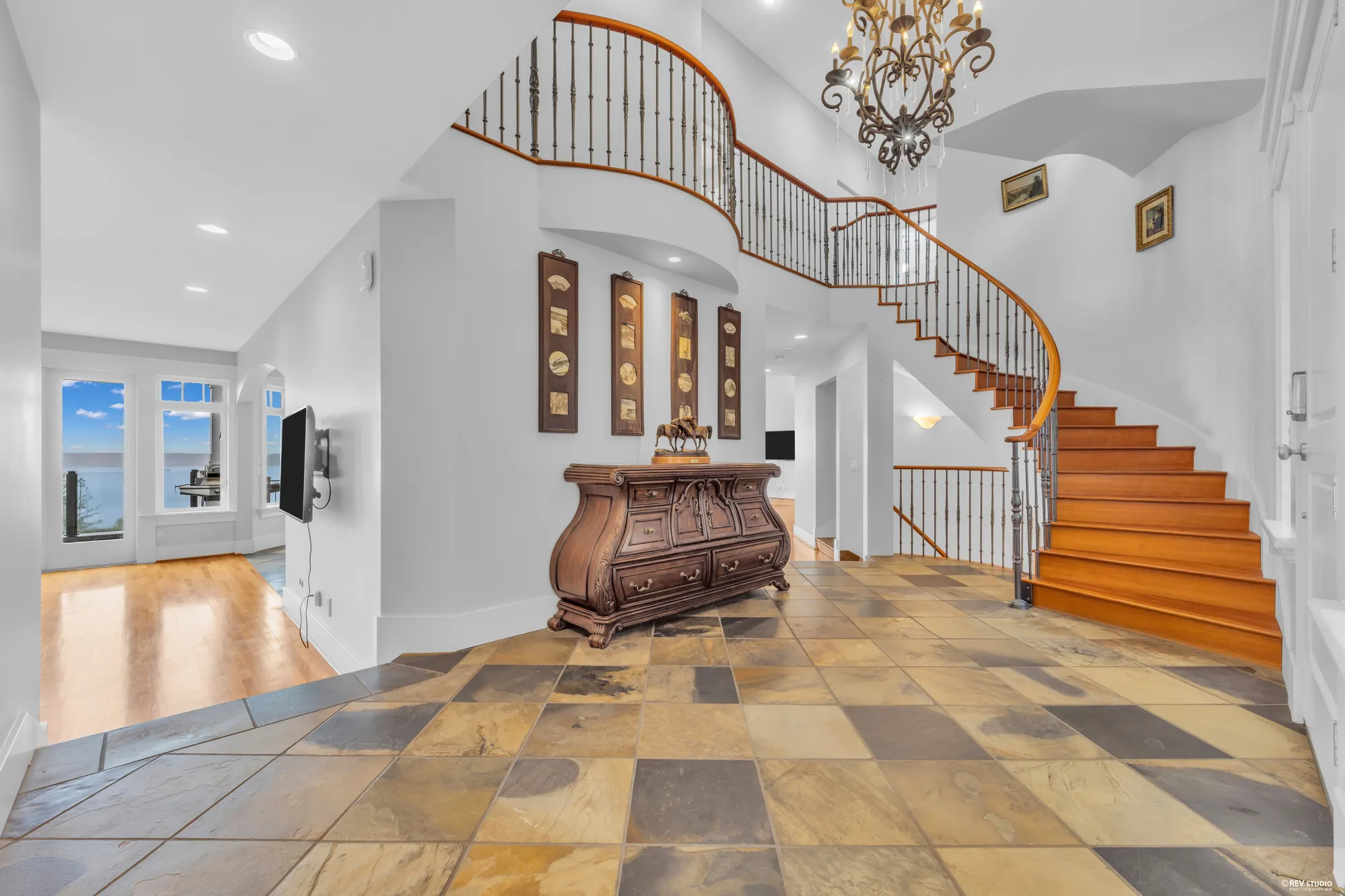 The foyer under a chandelier with a curved stair rising past the landing, slate laid in a diamond pattern underfoot