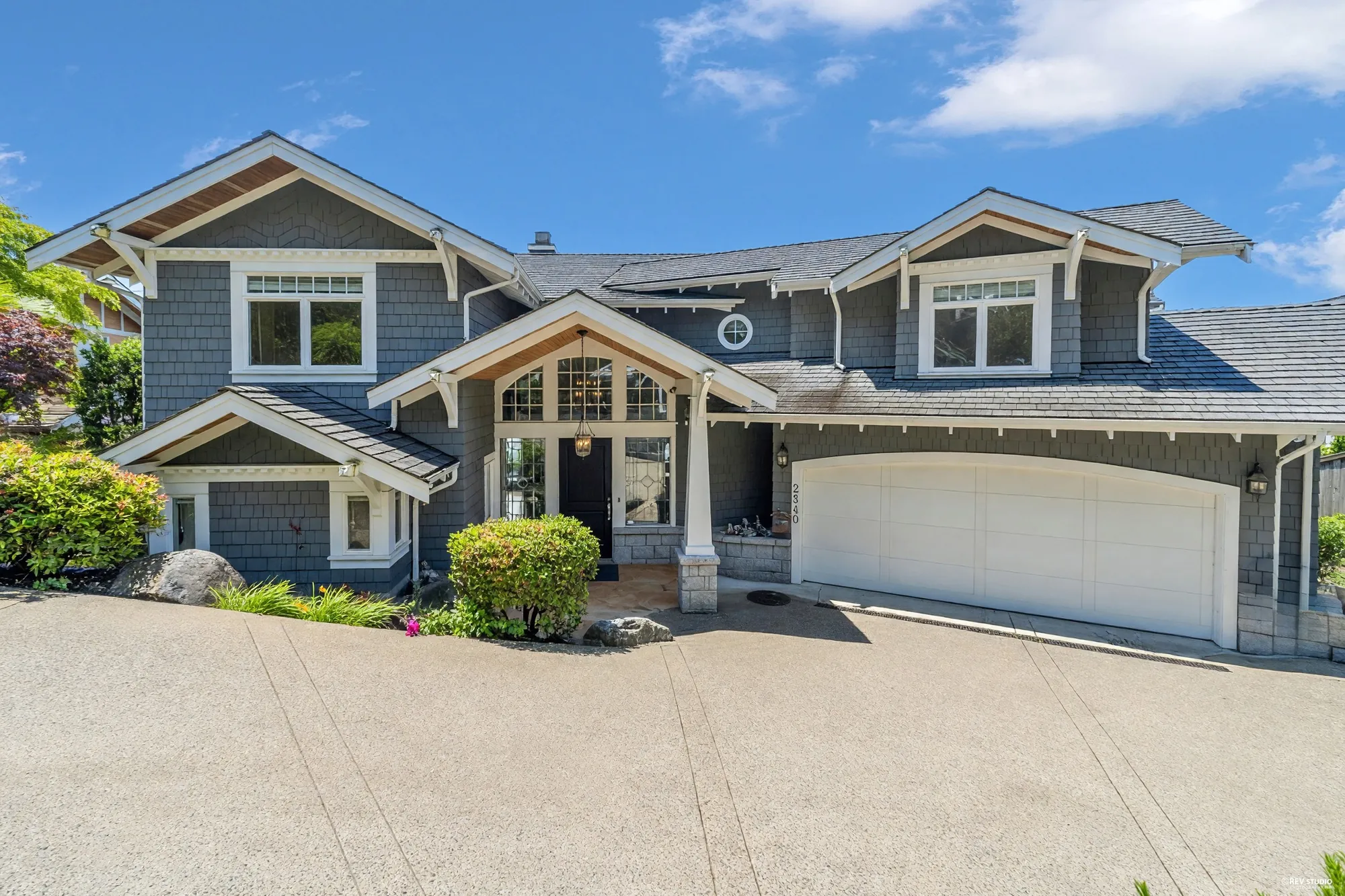 The front elevation in daylight: grey shingles, white trim, a timber-braced entry gable and the double garage