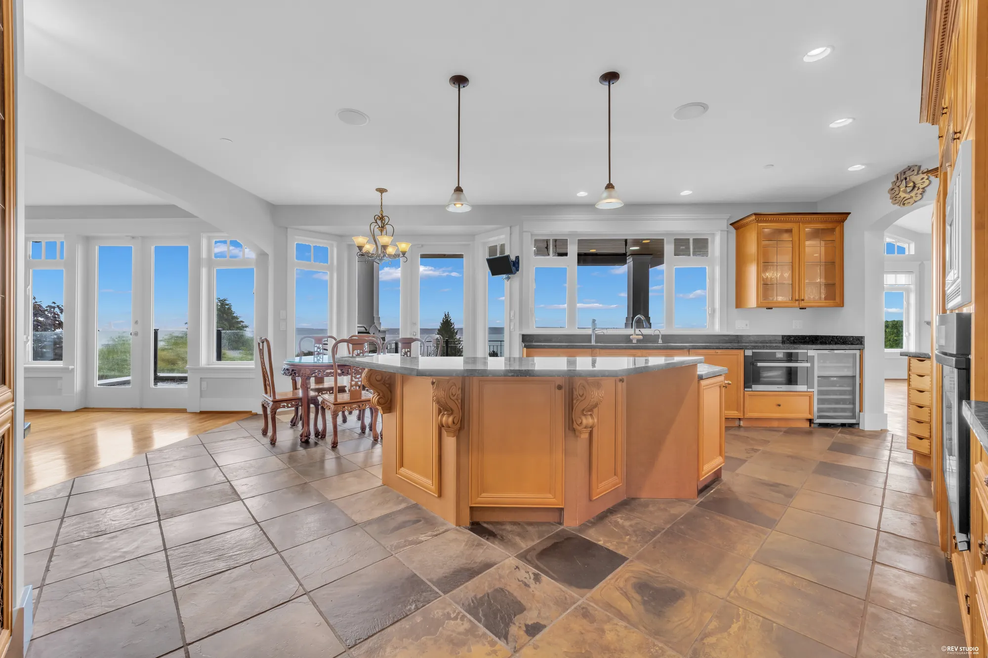 The kitchen island in maple with a granite top and a gas cooktop, glass-fronted cabinetry behind and the slate floor underfoot