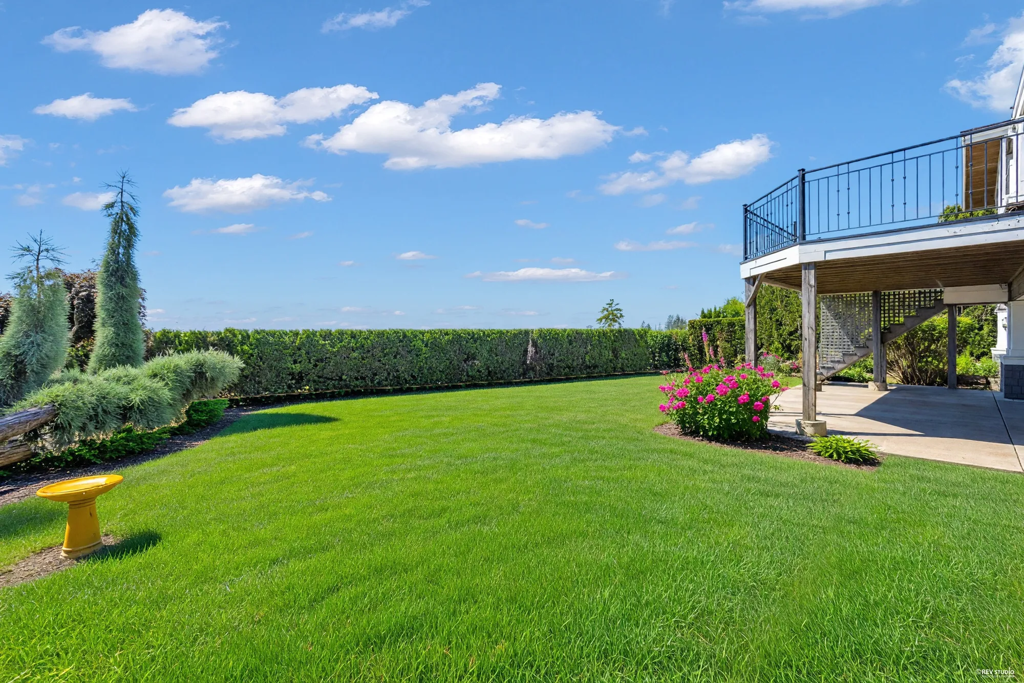 The flat back lawn looking along the boundary hedge, a flowering bed at one end and the patio at the other