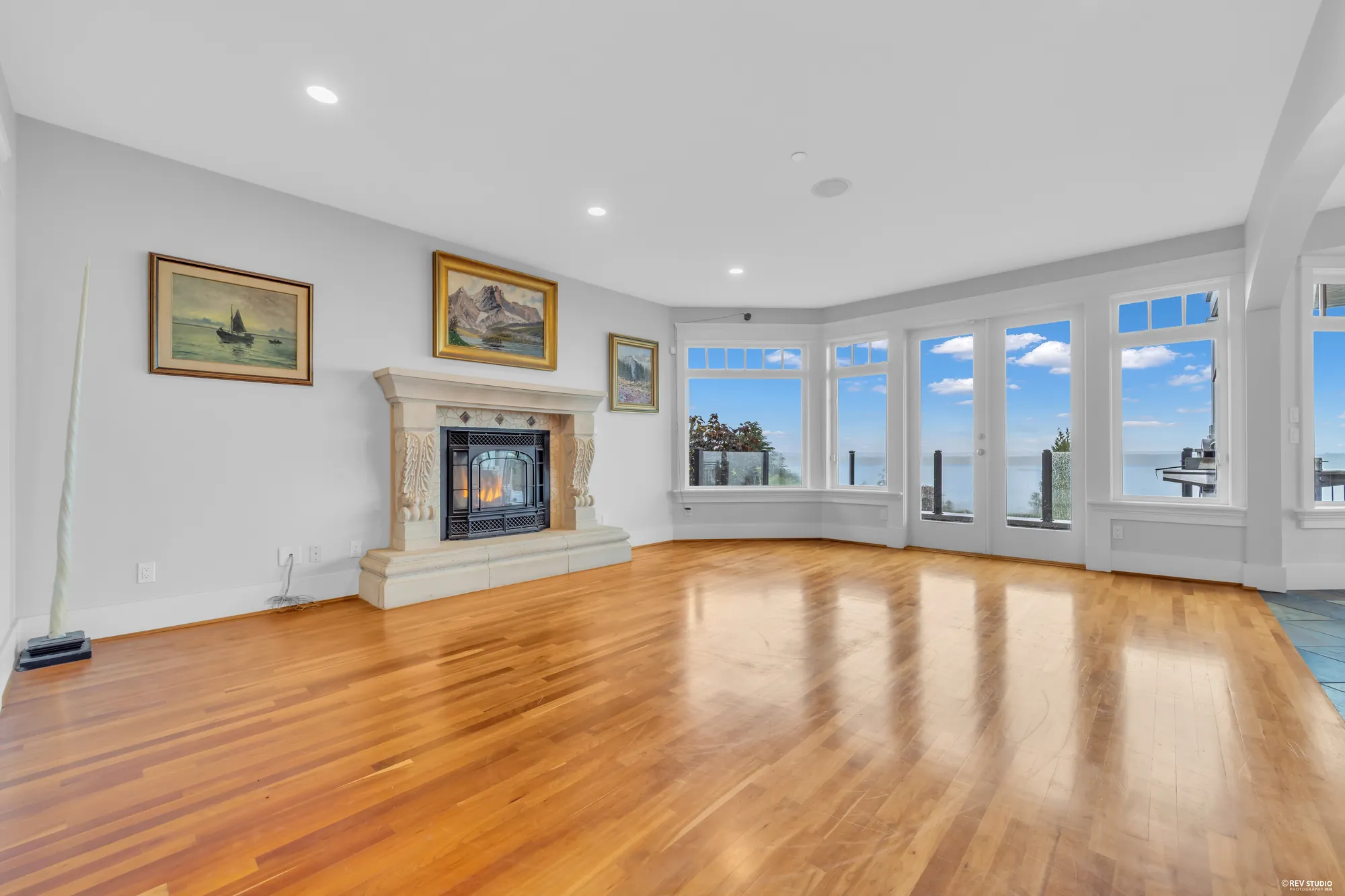 The living room with a carved stone fireplace between two windows and cherry floors running the length of the room