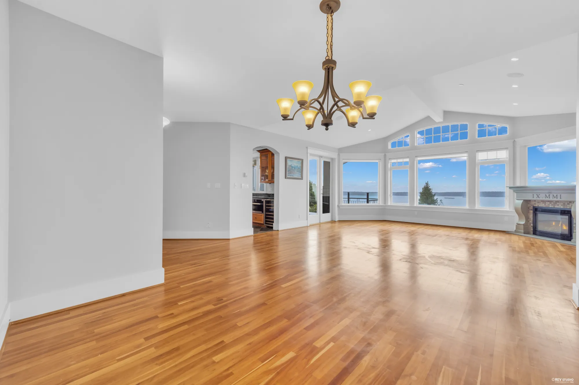 The living room with cherry floors running to a bank of windows on the view side, a fireplace at one end and the vaulted ceiling above