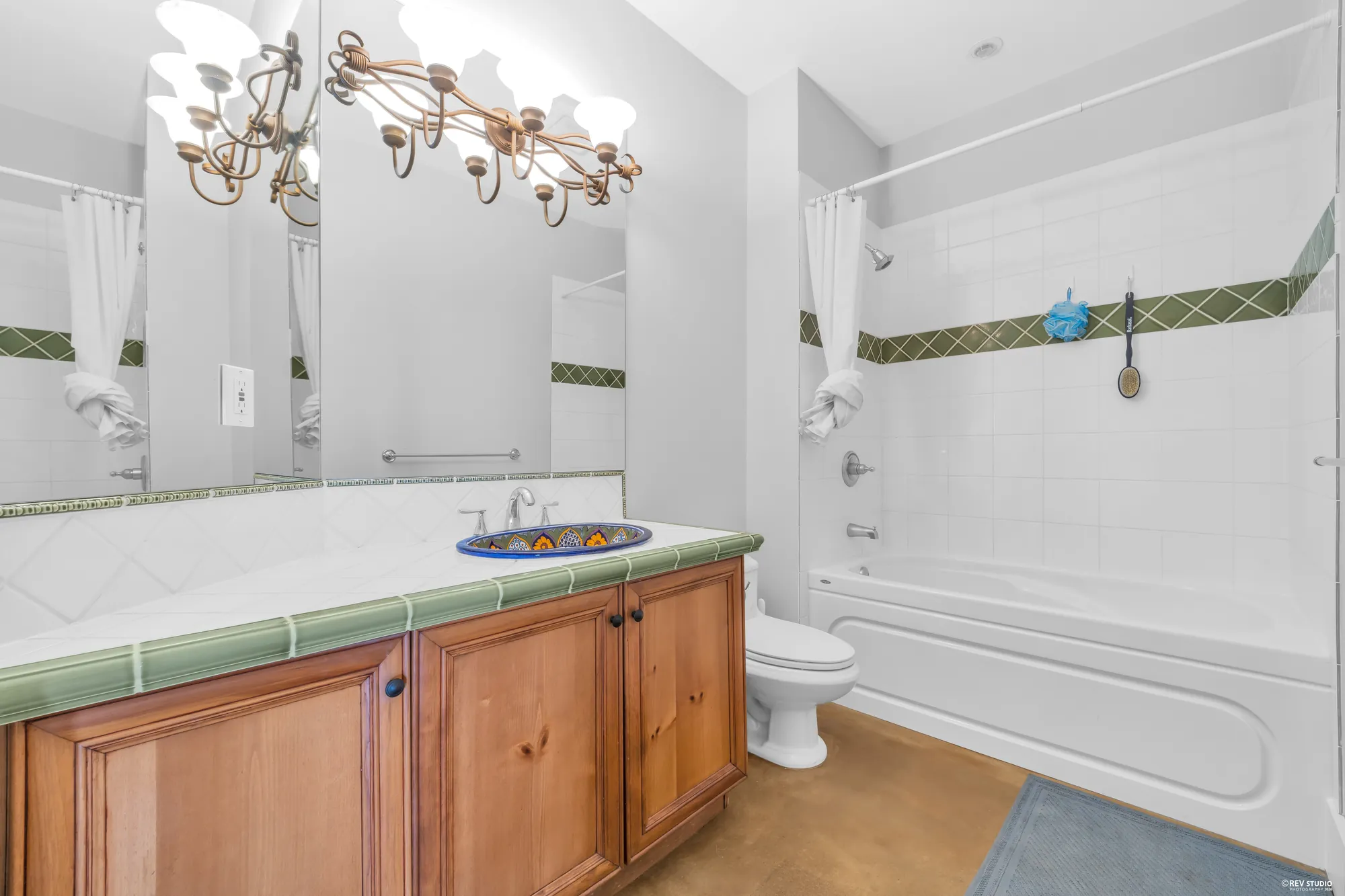 The lower bathroom with a tiled tub surround, a maple vanity and a chandelier