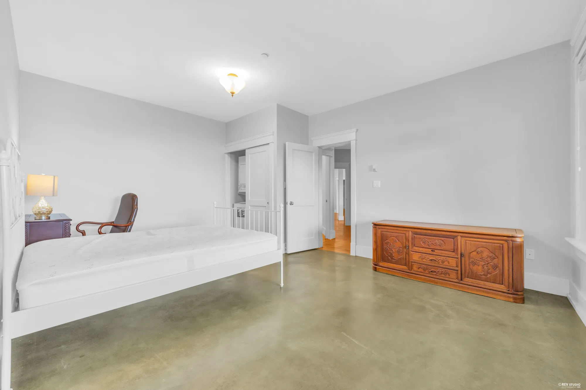 The lower bedroom from the far corner with a chair by the window and a chest against the wall