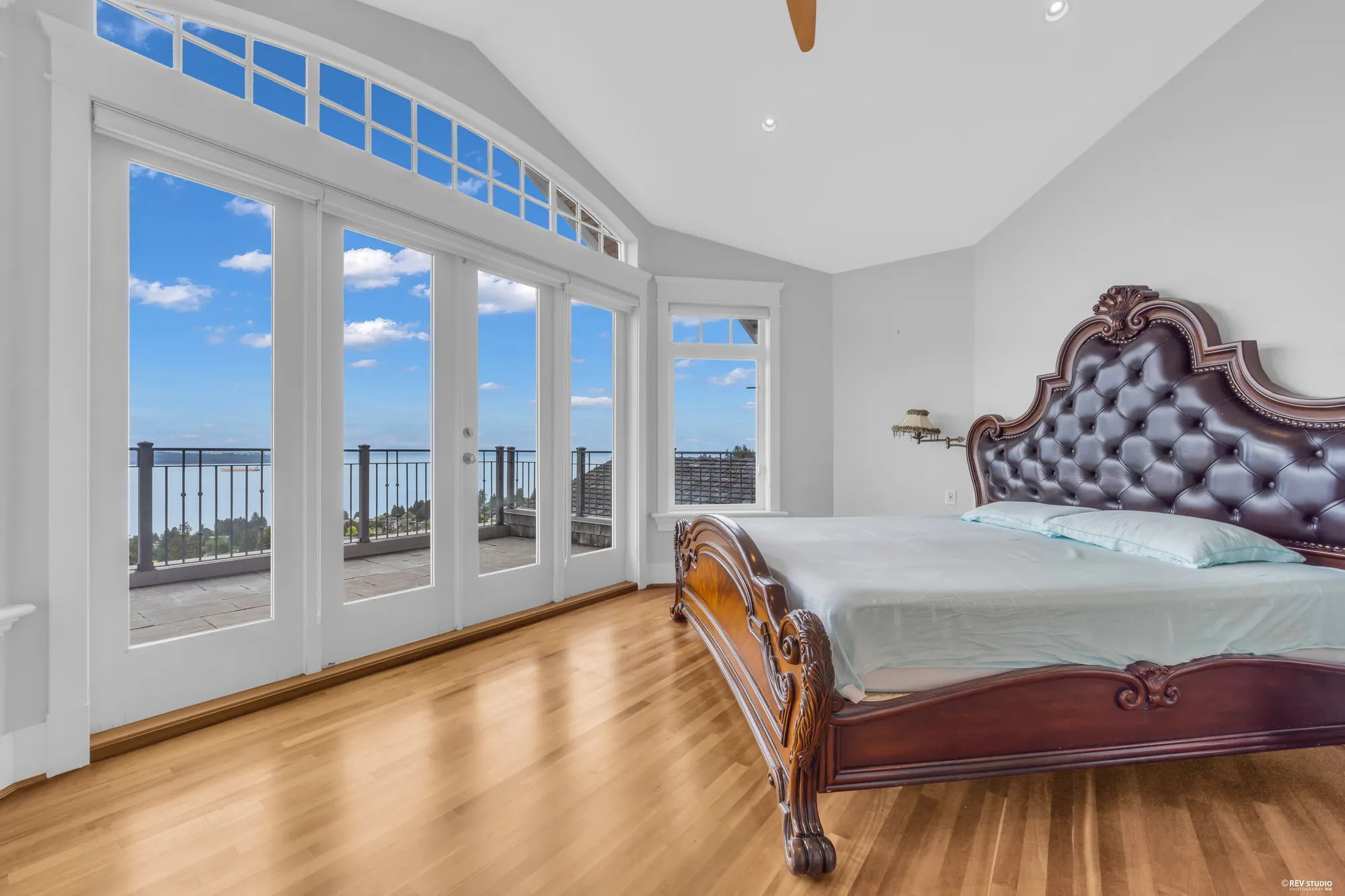 The primary bedroom in a bay of arched windows facing the water, cherry floors and a carved timber bed