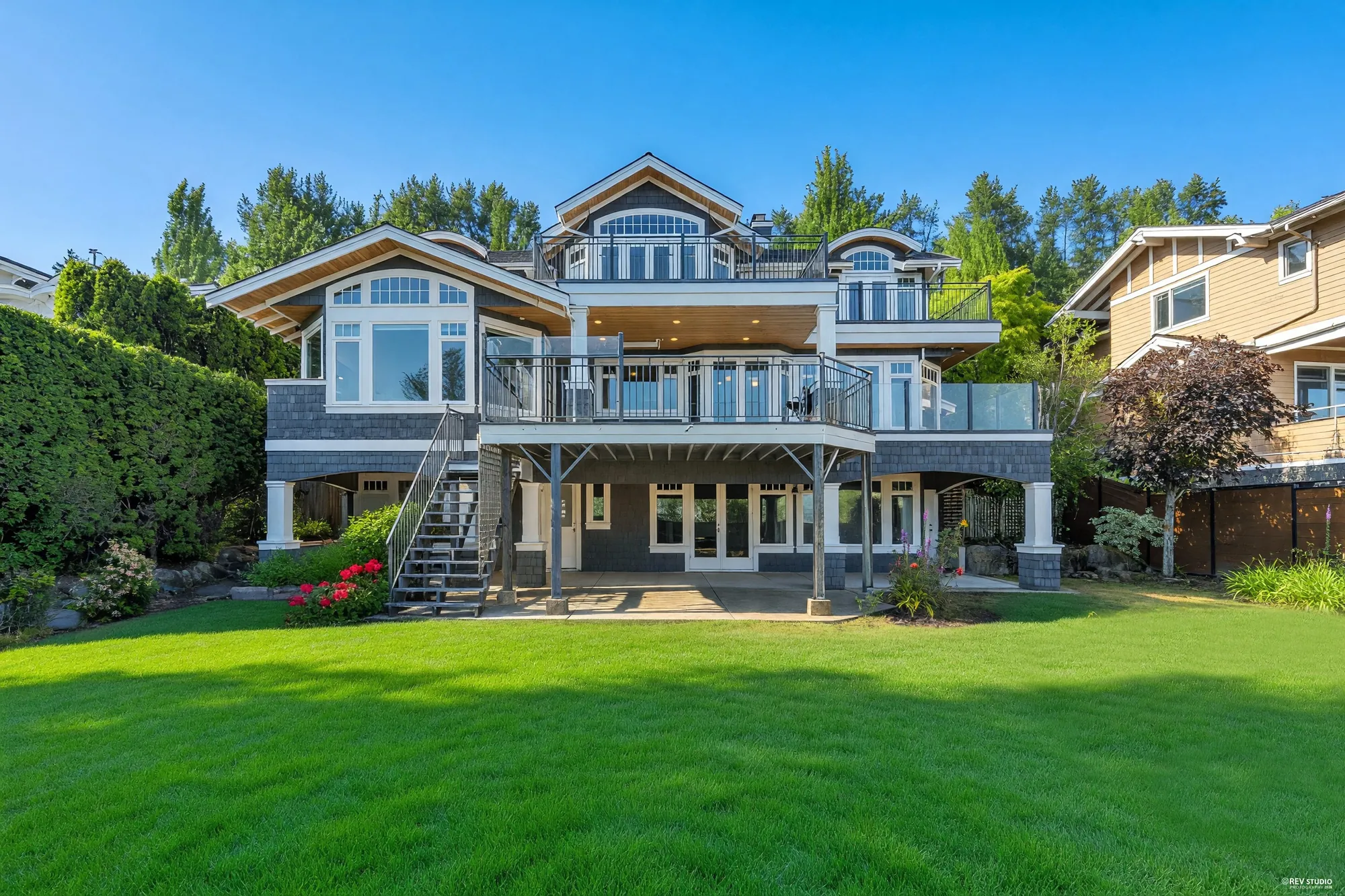 The back of the house from the lawn: three storeys of bay windows over a covered patio, with a stair down from the balcony