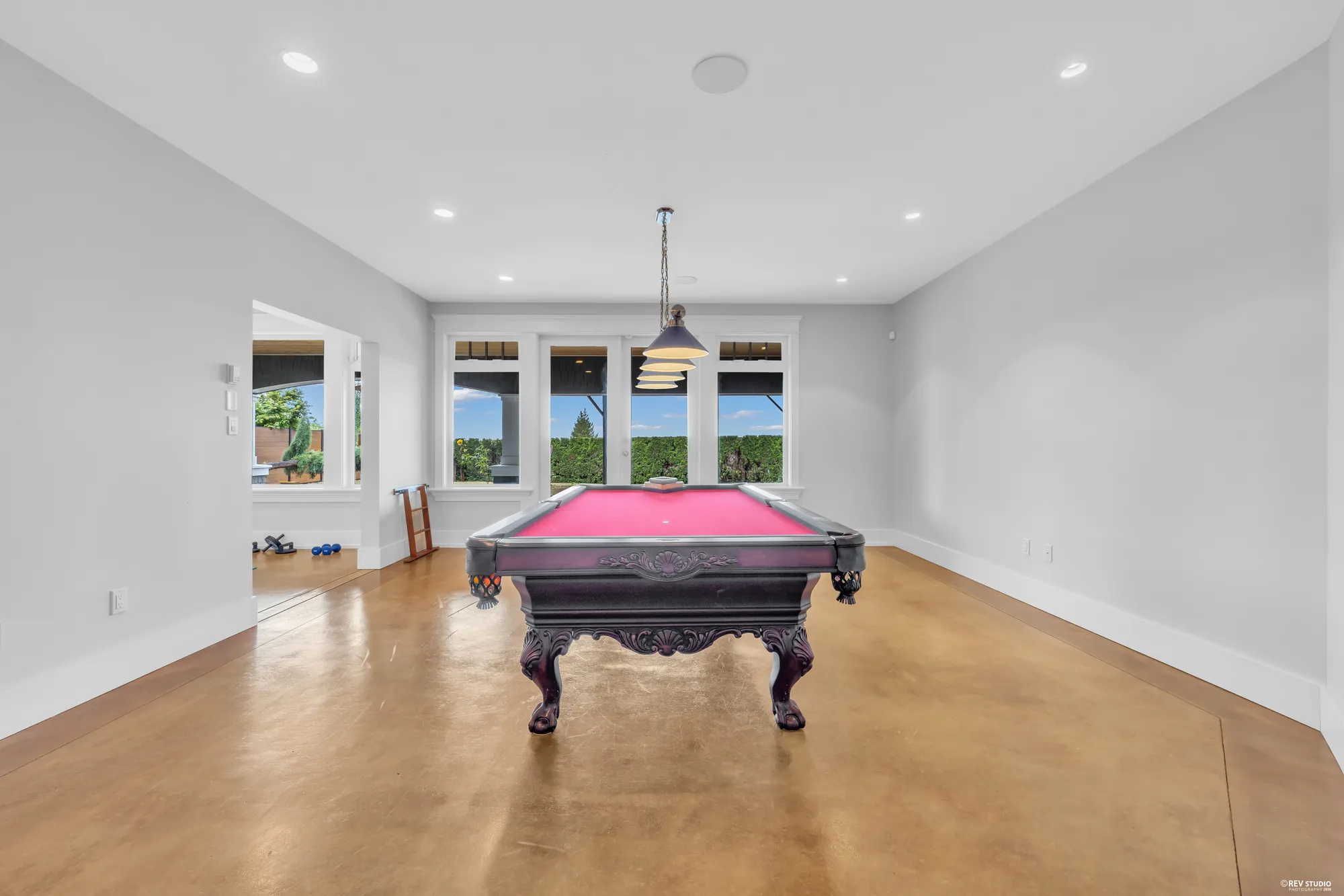 The recreation room with a full-size pool table on a polished concrete floor and windows at the far end