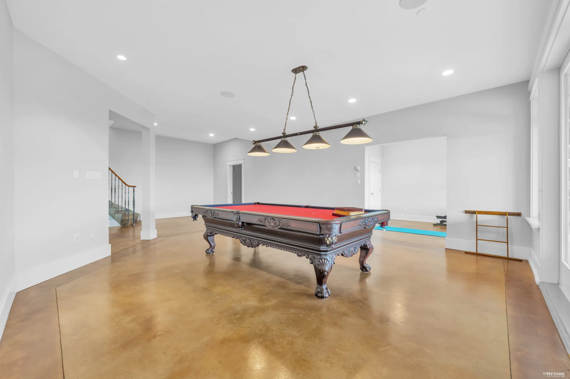 The recreation room under its linear pendant, the pool table on one side and the hall on the other
