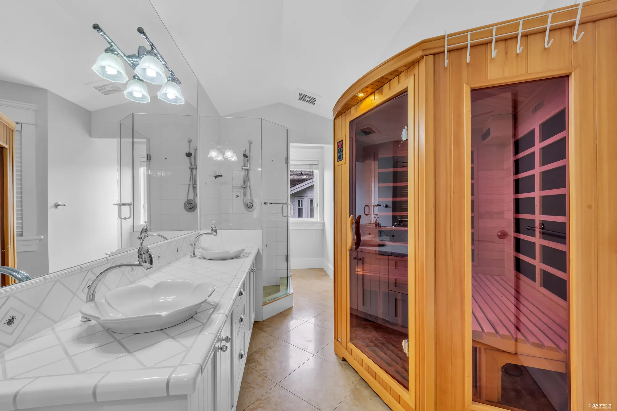 A bathroom with a cedar sauna cabin standing in the corner beside the shower and a twin vanity