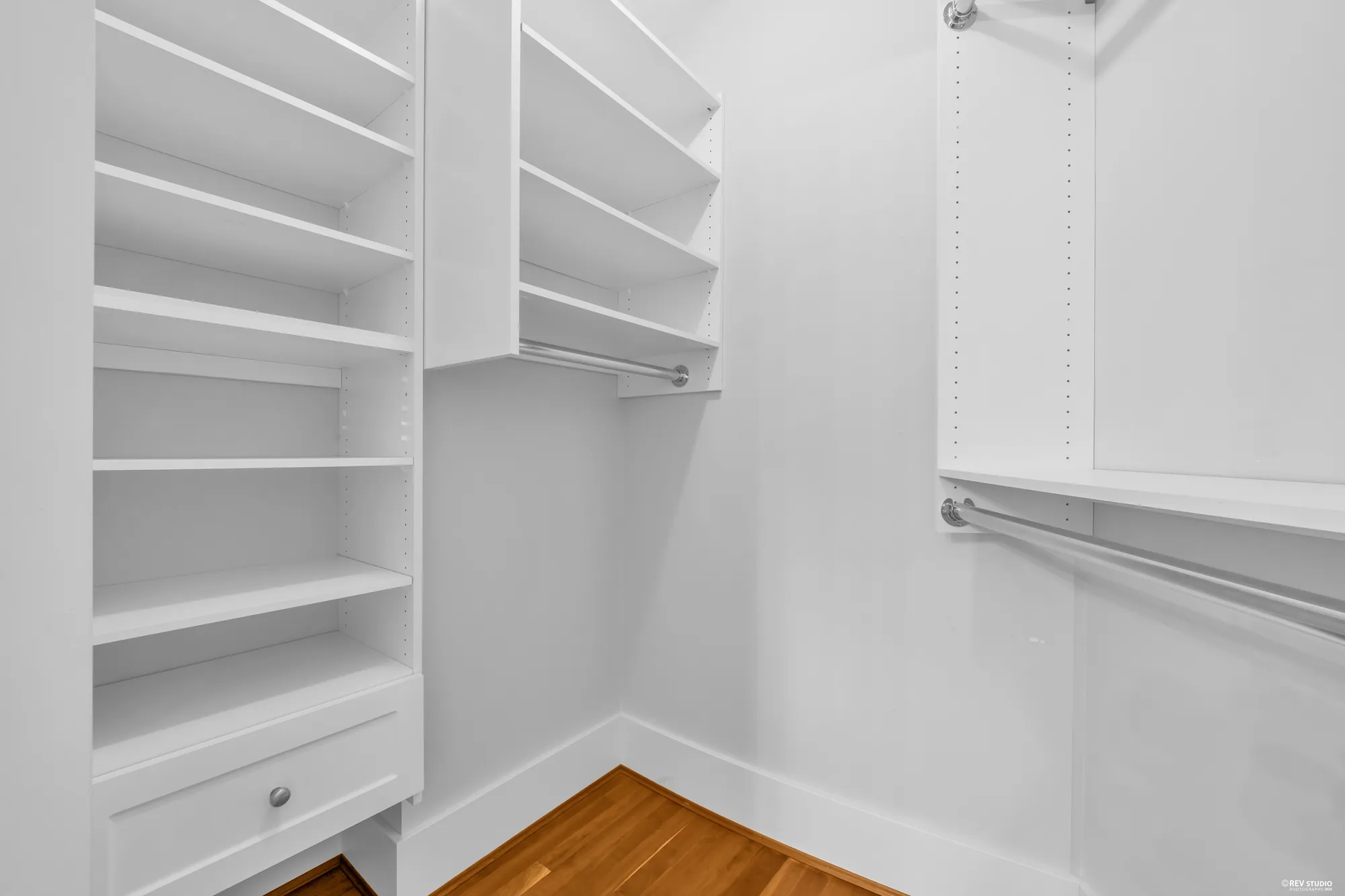 A fitted walk-in closet with white shelving and hanging rails on both sides